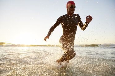 Male triathlete swimmer in wet suit running from ocean - CAIF05999