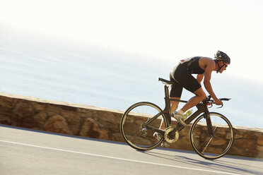 Male triathlete cyclist racing on ocean road - CAIF06001