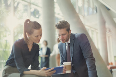 Business people drinking coffee and using digital tablet in office lobby - CAIF06029