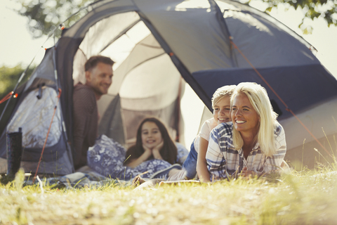 Lächelnde Familie entspannt sich vor dem sonnigen Zelt auf dem Campingplatz, lizenzfreies Stockfoto