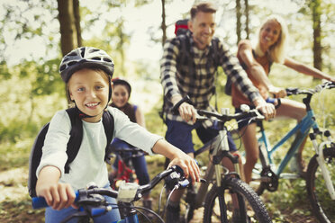 Porträt lächelndes Mädchen beim Mountainbiking mit Familie im Wald - CAIF06048