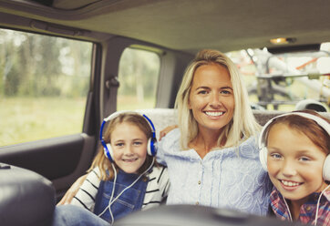 Portrait lächelnde Mutter und Töchter mit Kopfhörern auf dem Rücksitz eines Autos - CAIF06054