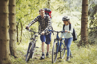 Vater und Tochter mit Rucksäcken auf Mountainbikes im Wald - CAIF06055