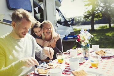 Happy family hugging and eating breakfast outside sunny motor home - CAIF06056