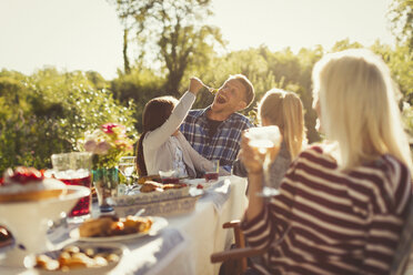 Playful daughter feeding father at sunny garden party patio table - CAIF06057