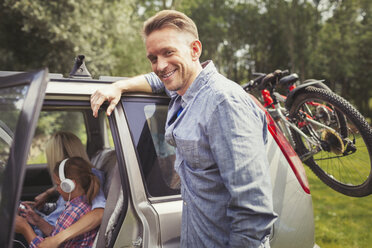 Portrait smiling father leaning on car with mountain bikes - CAIF06064