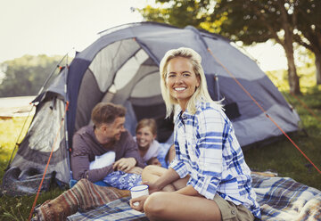 Porträt einer lächelnden Mutter, die mit ihrer Familie im Zelt auf dem Campingplatz Kaffee trinkt - CAIF06067