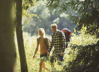 Paar mit Rucksäcken beim Wandern im sonnigen Wald - CAIF06071