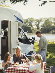 Familie genießt das Frühstück am Tisch vor dem sonnigen Wohnmobil - CAIF06072