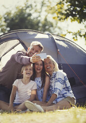 Happy family taking selfie with camera phone outside sunny campsite tent - CAIF06073