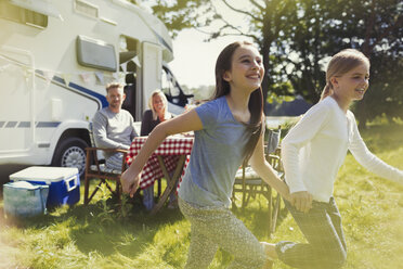 Playful sisters running and holding hands outside sunny motor home - CAIF06075