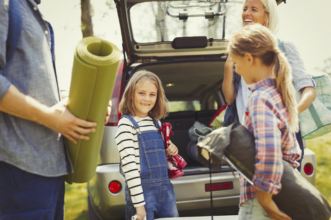 Portrait lächelndes Mädchen mit Familie beim Ausladen der Campingausrüstung aus dem Auto, lizenzfreies Stockfoto