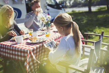 Girl using digital tablet at breakfast table outside sunny motor home - CAIF06083