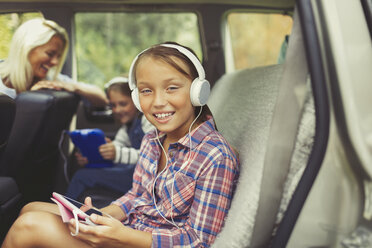 Porträt eines lächelnden Mädchens mit Kopfhörern, das ein digitales Tablet auf dem Rücksitz eines Autos benutzt - CAIF06084