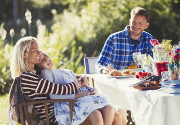 Lächelnde, liebevolle Familie genießt das Mittagessen am sonnigen Gartenparty-Terrassentisch - CAIF06085