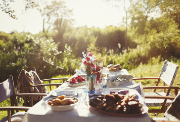 Essen und Blumenstrauß auf sonnigem Gartenparty-Terrassentisch - CAIF06088