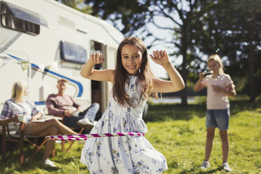 Portrait smiling girl spinning in plastic hoop outside sunny motor home - CAIF06091