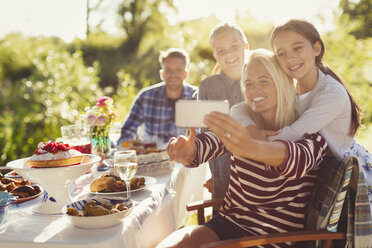 Mother and daughters taking selfie with camera phone at garden party patio table - CAIF06096