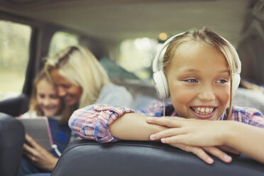 Lächelndes Mädchen, das auf dem Rücksitz eines Autos mit Kopfhörern Musik hört - CAIF06097