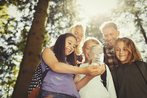 Familie hält Glas mit Schmetterling im sonnigen Wald, lizenzfreies Stockfoto