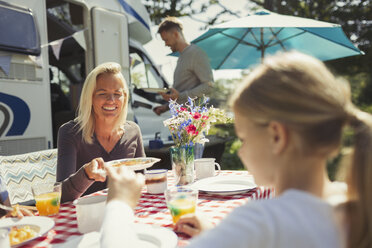 Smiling mother and daughter enjoying breakfast at table outside sunny motor home - CAIF06103
