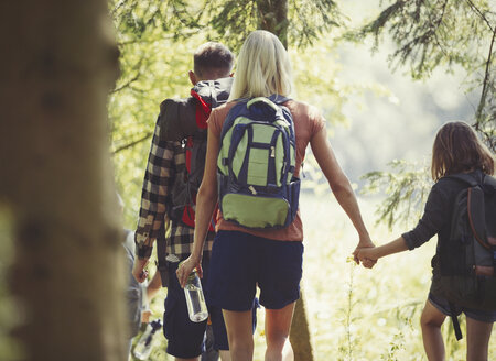 Mutter und Tochter mit Rucksäcken, die sich an den Händen halten, wandern im Wald - CAIF06106