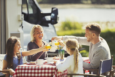 Familie stößt mit Kaffee und Orangensaftgläsern am Tisch vor dem sonnigen Wohnmobil an - CAIF06109