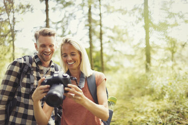 Smiling couple hiking, viewing digital SLR camera in woods - CAIF06114