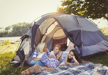 Mother and daughters talking and relaxing in tent at campsite - CAIF06116