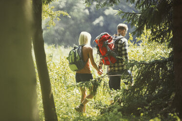 Couple with backpacks holding hands hiking in sunny woods - CAIF06117