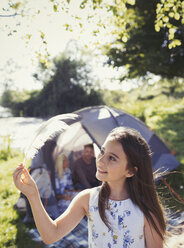 Neugieriges Mädchen hält eine Feder vor dem Zelt auf dem Campingplatz - CAIF06118