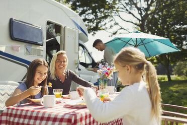 Familie genießt das Frühstück am Tisch vor dem sonnigen Wohnmobil - CAIF06119