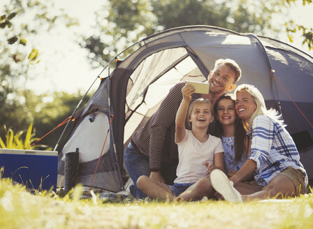Familie macht Selfie mit Fotohandy vor dem Zelt auf einem sonnigen Campingplatz - CAIF06120