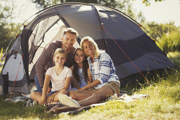 Portrait smiling family relaxing outside sunny campsite tent - CAIF06123