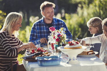 Family eating at sunny garden party patio table - CAIF06124
