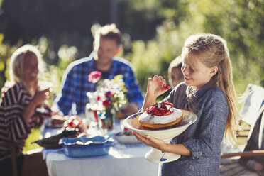 Mädchen hält Erdbeerkuchen am sonnigen Gartenparty-Terrassentisch - CAIF06125