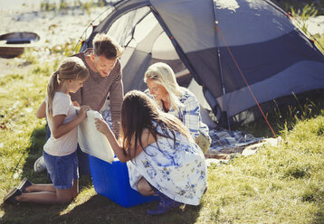 Familie öffnet Kühlbox vor dem sonnigen Zelt auf dem Campingplatz - CAIF06129