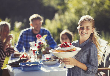 Porträt lächelnd Mädchen serviert Erdbeerkuchen an die Familie im sonnigen Garten Partei Patio Tisch - CAIF06131