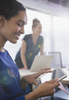 Lächelnde Geschäftsfrau mit digitalem Tablet in einem Konferenzraum - CAIF06147