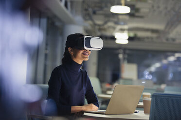 Geschäftsfrau mit Virtual-Reality-Simulator am Laptop in einem dunklen Büro - CAIF06189