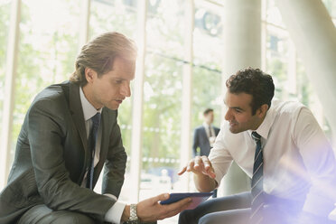 Businessmen meeting using digital tablet in office lobby - CAIF06201