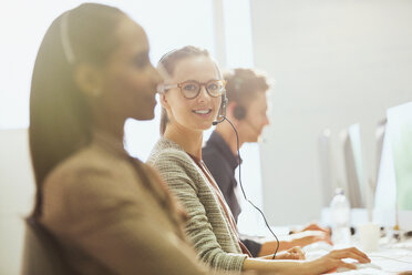 Portrait smiling female telemarketer wearing headset at computer in office - CAIF06203