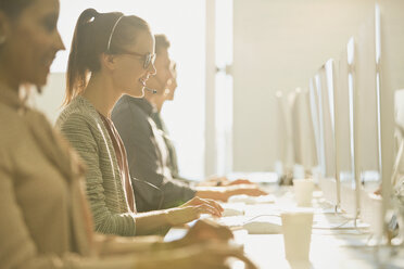 Weibliche Telefonverkäuferin mit Headset, die in einem sonnigen Büro am Computer telefoniert - CAIF06210