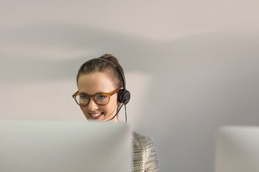 Lächelnde Telefonverkäuferin mit Headset, die am Computer im Büro telefoniert - CAIF06215