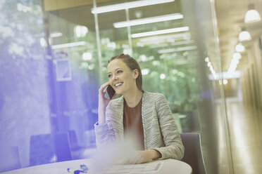 Smiling businesswoman talking on cell phone in conference room - CAIF06223