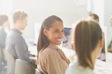 Smiling female telemarketers wearing headsets talking in sunny office - CAIF06226