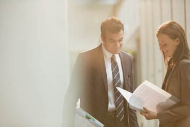 Businessman and businesswoman reviewing paperwork in office lobby - CAIF06231