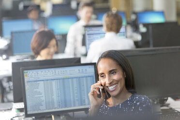 Smiling businesswoman talking on cell phone at computer in office - CAIF06236