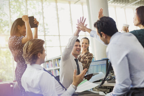 Business people high-fiving and celebrating in office - CAIF06241