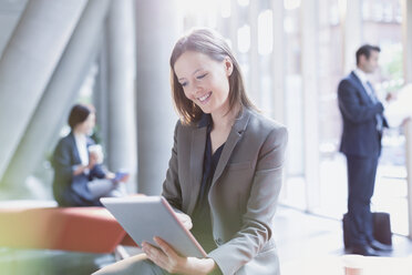 Smiling businesswoman using digital tablet in sunny office lobby - CAIF06249
